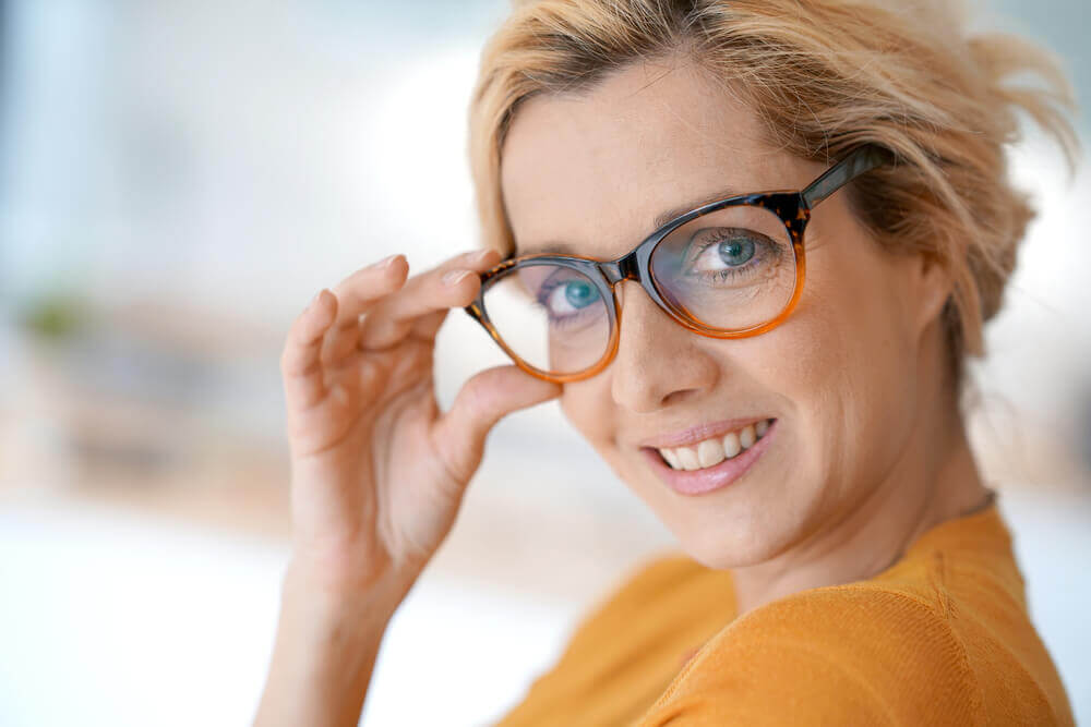 Confident woman in her 50s with blonde hair, wearing fashionable tortoiseshell glasses, smiling warmly. An ideal representation of trendy glasses for women over 50, combining modern style with age-appropriate design.